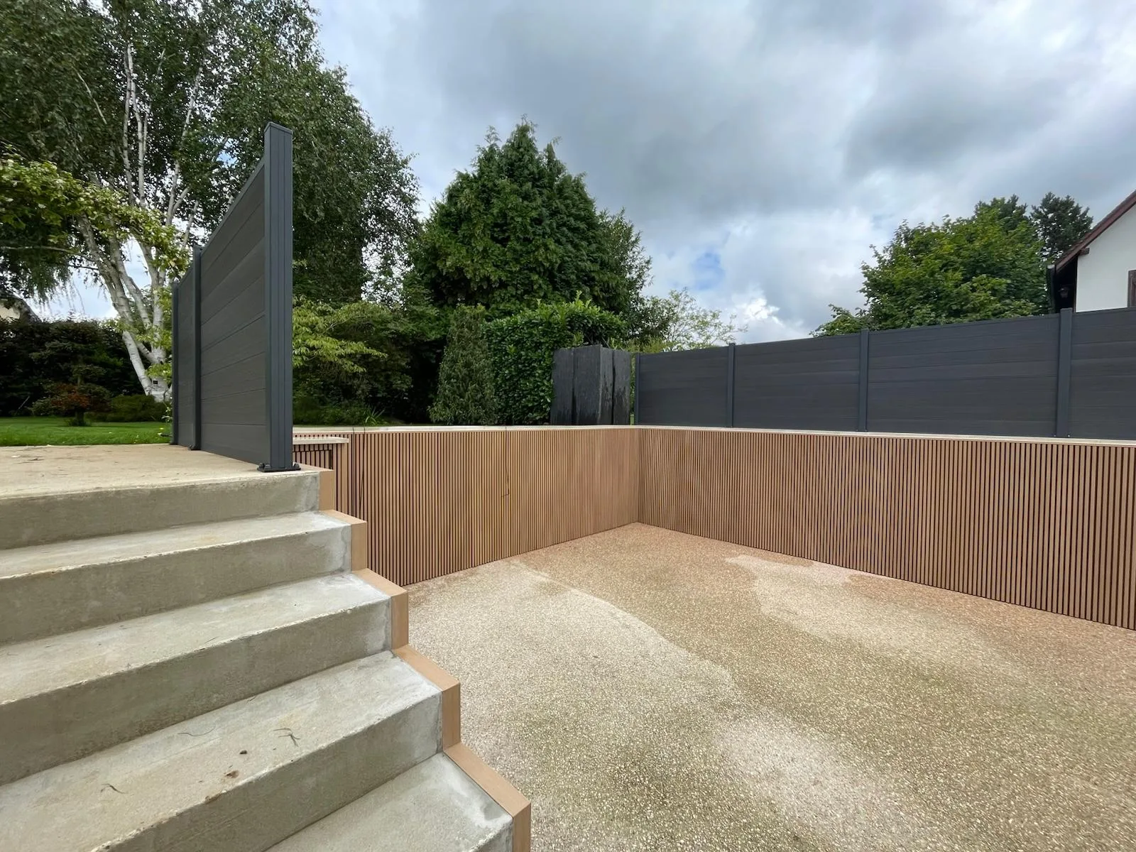 Jardin moderne avec espace clôturé et accents en bois sous un ciel nuageux.