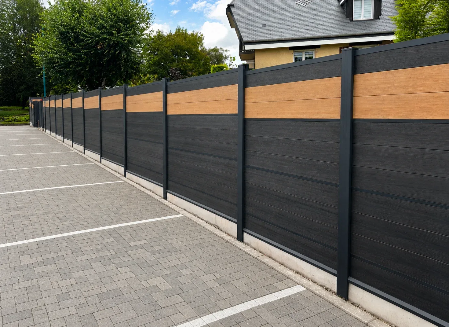 Clôture design bois et sombre près d'un parking sous ciel dégagé.