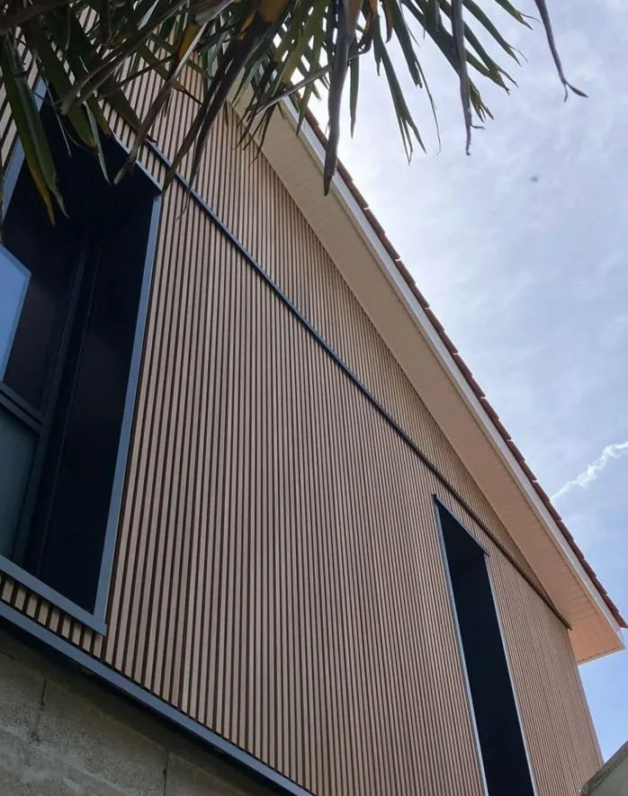 Façade moderne d'un bâtiment avec des lames verticales en bois sous un ciel dégagé